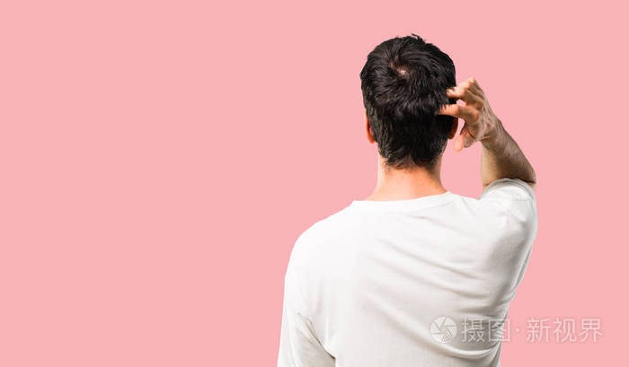 一个年轻的年轻人,穿着白色衬衫,仰着头,在孤立的粉红色背景下挠头