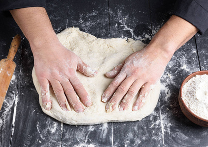 s hands knead a round piece of dough for making pizza, top view