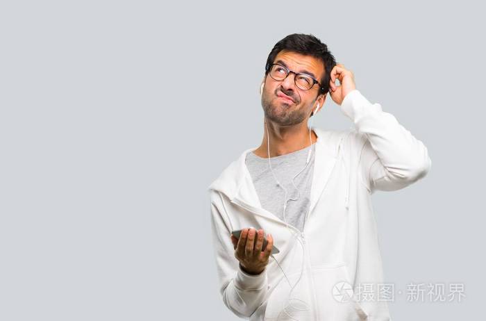 戴眼镜和听音乐的人在灰色背景上挠头时会产生怀疑和迷惑的面部表情