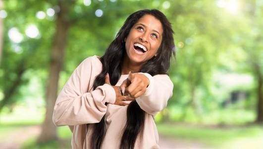 年轻的美国黑人妇女用手指指着某人，在户外大笑