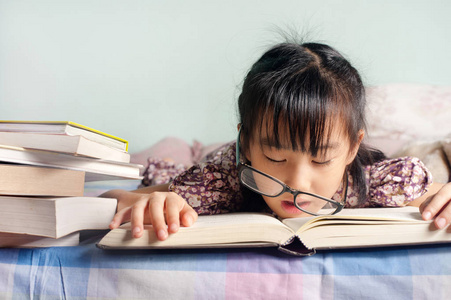 亚洲孩子睡在床上看书. 戴眼镜的女孩研究睡眠选择性聚焦照片