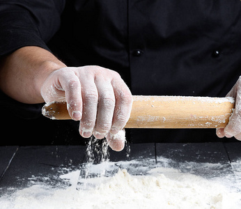 厨师手里拿着一根木擀面杖，白色的小麦粉散落在桌子上