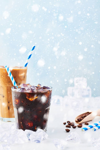 冬天喝冰咖啡在玻璃和冰咖啡与奶油在一个高玻璃咖啡豆和吸管周围的白色大理石桌子上与雪。 复制空间。