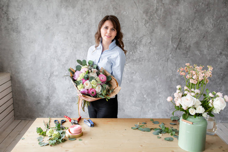 年轻友好的微笑的女性花卉艺术家看着相机, 手里拿着一束豪华的花束。专业花店在花店制作一束粉红色的兰诺库勒斯和牡丹