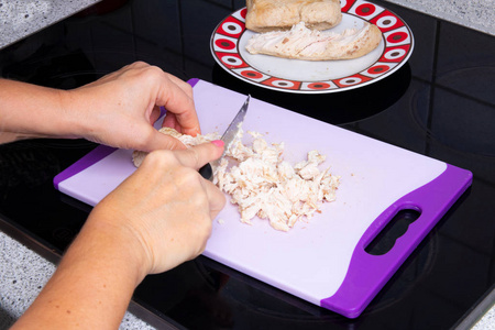 用手中的一把刀把熟火鸡肉切在切割板上。 健康食品概念。
