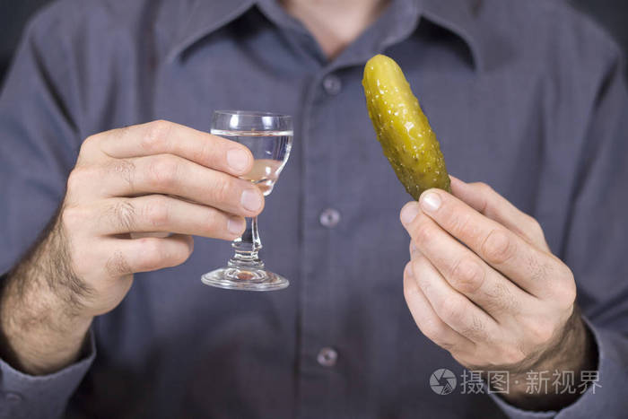 男人一只手拿着一杯伏特加,另一只手拿着一根腌制的黄瓜.