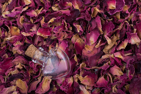 干燥玫瑰花瓣背景的心形瓶子图片
