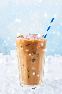 冬天喝冰咖啡，在一个高大的玻璃杯里，用稻草包围在白色大理石桌子上，蓝色背景下有雪。 文本的选择性焦点复制空间。