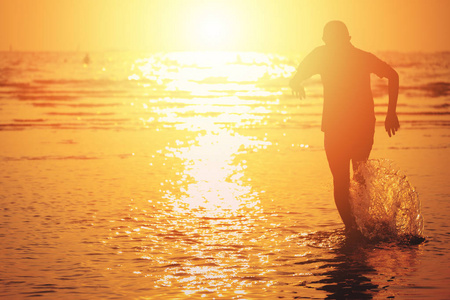 孩子跑向大海，水在夏天随着日落飞溅。