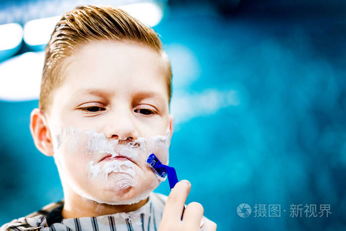 一个带着骄傲表情的小男孩像成年男人在蓝色背景下刮脸一样