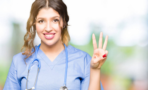年轻的成年医生女士穿着医疗制服，用手指举着第三个手指，微笑着自信和快乐。