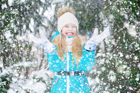 一个女孩举起双手，举起雪，在冬天的森林里笑。