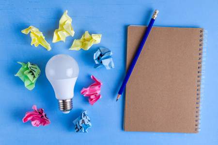 观念概念。 新主意。 彩色皱褶纸球笔记本和灯泡在蓝色背景。 开始吧。 复制空间