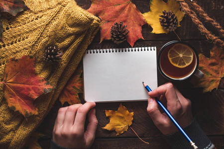 温暖的针织毛衣松果，一杯热茶与柠檬和秋天枫叶在木制背景。 秋天的衣服。 复制空间