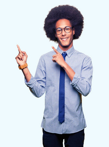 年轻的非裔美国商人带着非洲头发，戴着眼镜，微笑着看着相机，两只手和手指指向一边。