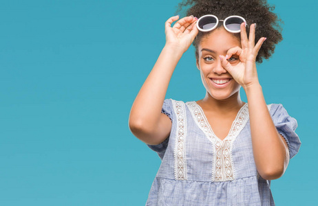 年轻的非洲美国妇女戴着眼镜，在孤立的背景下做着OK的手势，用手微笑的眼睛透过手指看着幸福的脸。