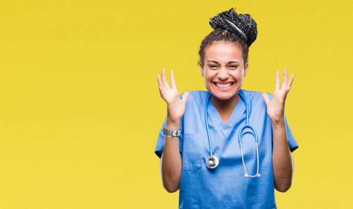 年轻的辫子非裔美国女孩专业外科医生在孤立的背景下庆祝疯狂和疯狂的成功，举起手臂和闭上眼睛尖叫兴奋。 赢家概念
