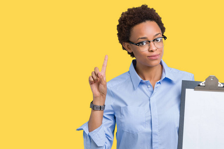 年轻的非裔美国人的商界女性拿着剪贴板，在孤立的背景下惊讶地发现了一个想法或问题，手指着幸福的脸第一