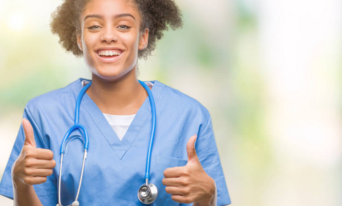 年轻的AFRO美国医生女士在孤立的背景下成功的标志，用手竖起大拇指，微笑和快乐地做积极的手势。 用欢快的表情看着相机，胜利者的手