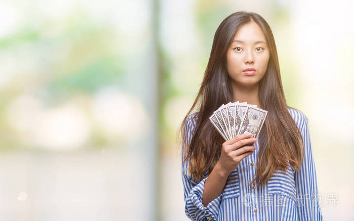 年轻的亚洲女人在孤立的背景上持有美元，聪明的脸上有自信的表情，严肃的思考