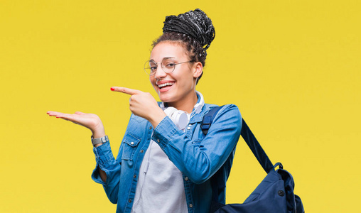 年轻的辫子非裔美国学生女孩穿着背包在孤立的背景上惊讶和微笑的相机，同时呈现手和手指。