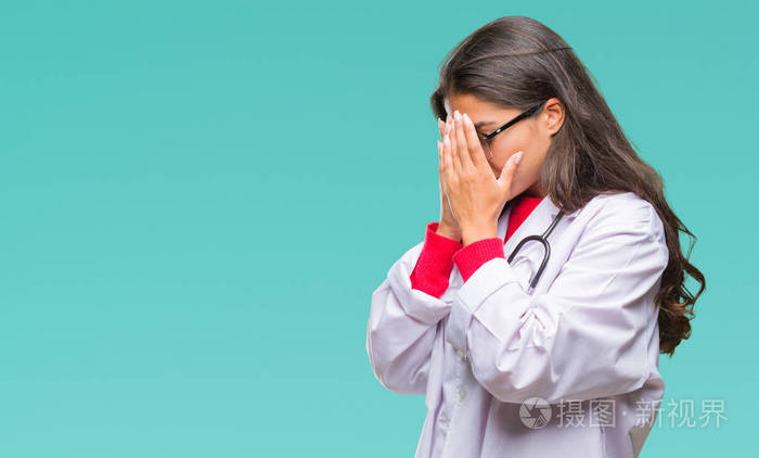 年轻的阿拉伯医生女人在孤立的背景上,悲伤的表情覆盖着脸,双手哭泣.