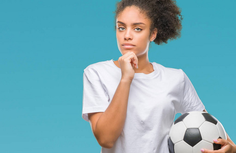 年轻漂亮的非洲裔美国人抱着足球在孤立的背景下严肃的脸思考问题非常困惑的想法