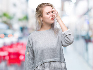 年轻的金发女人在孤立的背景上闻到一些臭味和令人恶心的难以忍受的气味，用手指在鼻子上屏住呼吸。 难闻的概念。