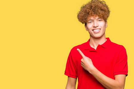 年轻的帅哥，一头非洲发，穿着红色的T恤衫，脸上带着微笑，用手和手指指向一边，脸上带着快乐和自然的表情