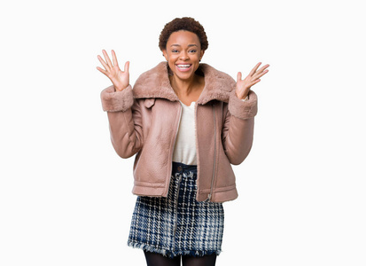 年轻的非裔美国妇女穿着冬天的外套，在孤立的背景下庆祝疯狂，并惊讶于成功，举起手臂睁开眼睛，尖叫兴奋。 赢家概念