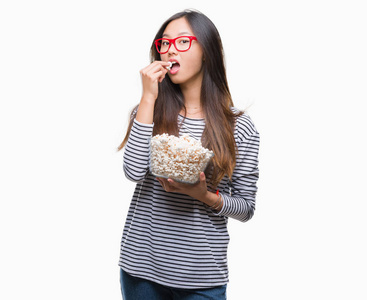 年轻的亚洲女人在孤立的背景下吃爆米花，聪明的脸上有自信的表情，严肃的思考