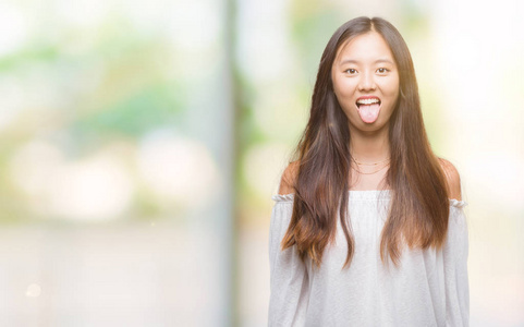 年轻的亚洲女人在孤立的背景下伸出舌头，以有趣的表情高兴。 情感概念。