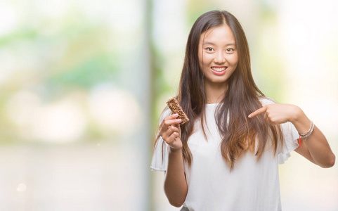 年轻的亚洲女人吃巧克力，精力充沛，在孤立的背景上，惊讶的脸指着自己