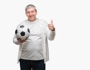 英俊的老人手里拿着足球球在孤立的背景下快乐地大笑着做着好的标志，用手指竖起大拇指，好的标志