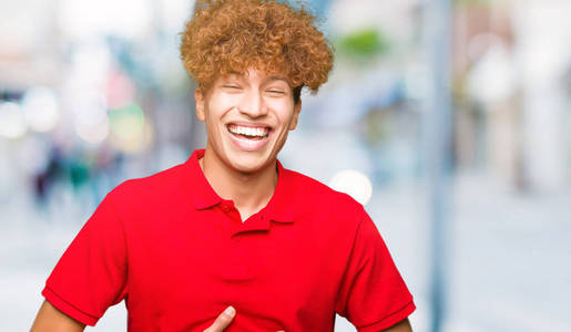 年轻的帅哥，头发是非洲的，穿着红色的t恤，笑得很大声，因为有趣的疯狂笑话。开心的表情。