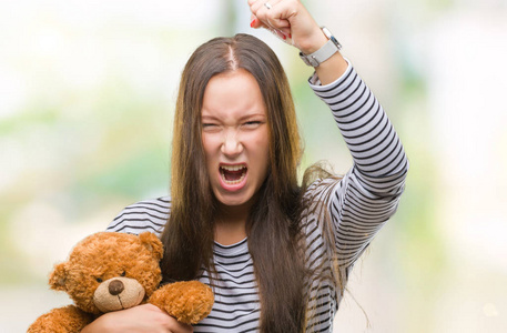 年轻的白种人女人抱着玩具熊在孤立的背景下,愤怒和沮丧地大喊大叫