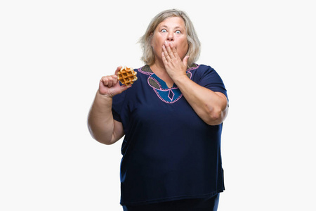 高年级加码的白种人女人在孤立的背景罩嘴上吃华夫饼,手因错误而震惊
