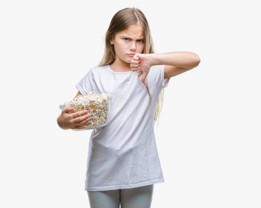 年轻漂亮的女孩在吃爆米花零食时，脸上带着愤怒的表情，消极的表情表示不喜欢，拇指向下，拒绝的概念
