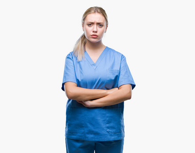 年轻的金发外科医生，女人穿着医疗制服，在孤立的背景怀疑和紧张的不赞成的表情在脸上交叉的手臂。 消极的人。