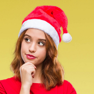 年轻漂亮的女人在孤立的背景上戴着圣诞帽，手拿下巴，想着问题，沉思的表情。 带着体贴的脸微笑。 怀疑概念。
