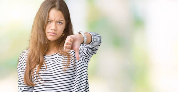 年轻漂亮的黑发女人穿着条纹毛衣，在孤立的背景上看起来不高兴和愤怒，表现出拒绝和消极的拇指向下的手势。 不好的表情。