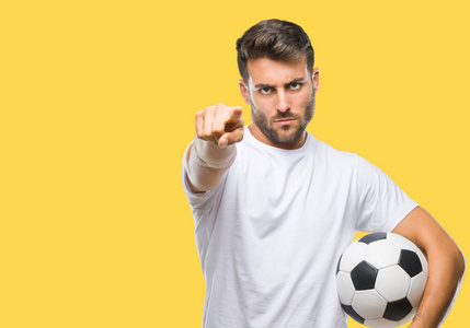 年轻的帅哥把足球球举在孤立的背景上，手指指向相机，并向你手势正面和自信的手势