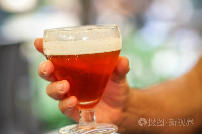 一只手拿着装满红啤酒的杯子