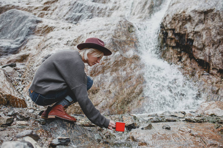 有杯子的漂亮女旅行者在瀑布里打水漂亮的瀑布景观有