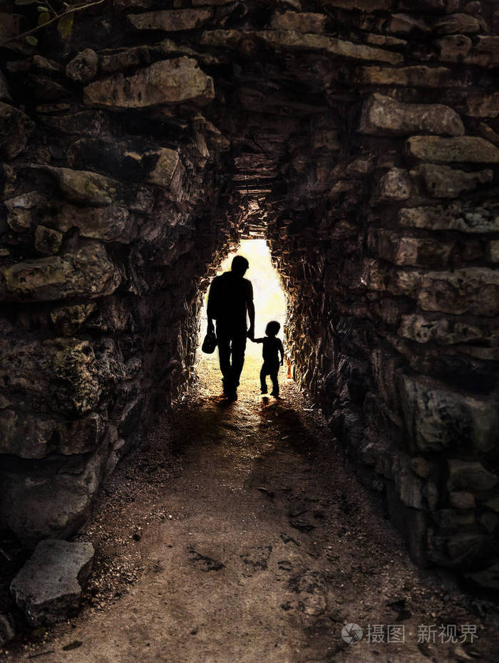 在一个小而黑暗的石头隧道背光中父子的轮廓在墨西哥的tulum拍摄的