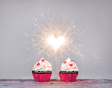 两个情人节奶油杯蛋糕与火花创造心形庆祝爱情概念
