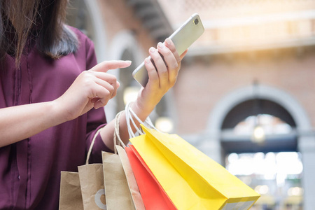 女人在商场里拿着纸袋看手机，一边享受一天的购物