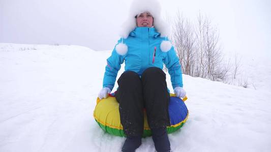 快乐的女孩在雪橇上在雪地上滑行, 美丽的年轻女子在雪中滑落在充气雪管上, 挥动着她的手。冬天在公园里玩圣诞节的女孩