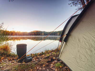 清晨湖边的绿色野营帐篷。 黎明的阳光照耀着森林山