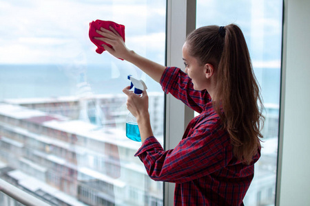 穿着衬衫,拿着一块抹布和一个用来清洗眼镜的喷雾剂在房子里擦窗户